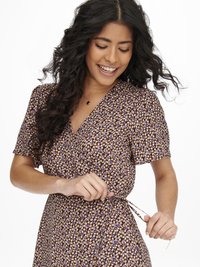 Vestido com padrão floral em tons de roxo, com mangas curtas, ajustado na cintura. Tecido macio com uma textura suave, apresentando um decote em V e um detalhe de laço.