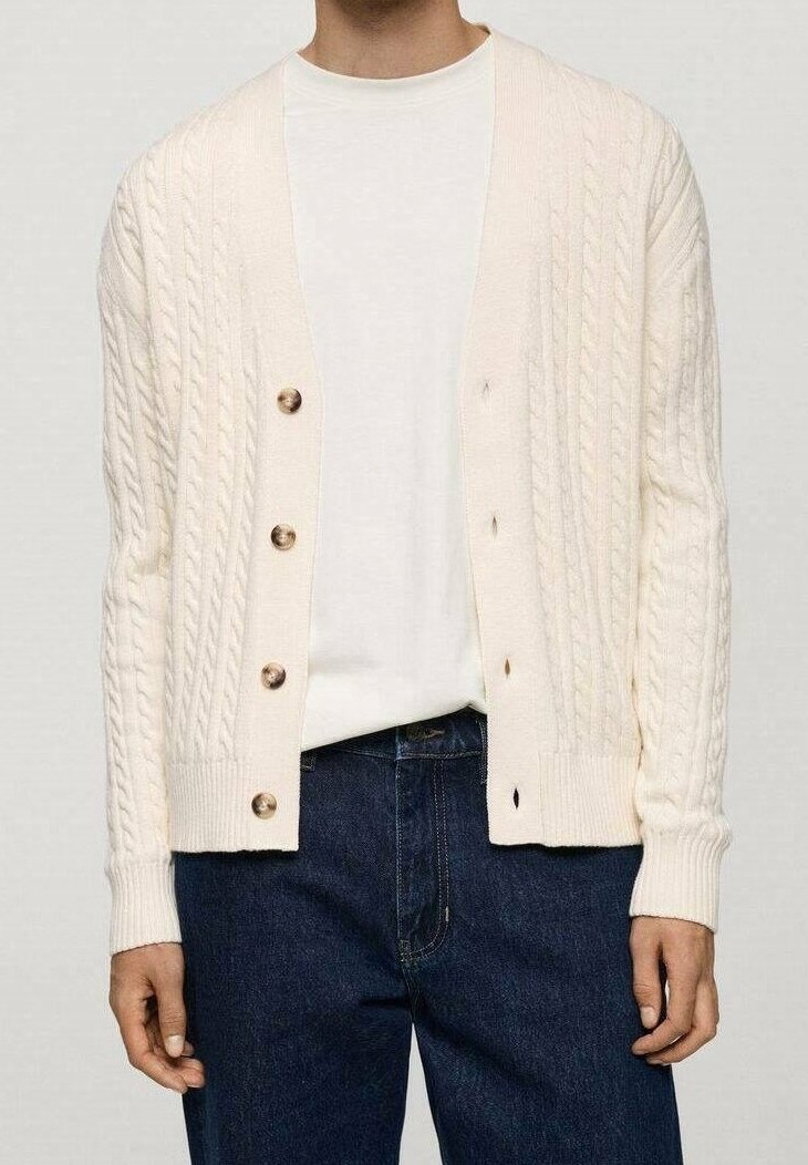 Cream cable-knit cardigan with a relaxed design, featuring six brown buttons, ribbed cuffs, and hem; worn over a plain white shirt.