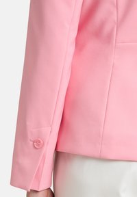 Lichtroze blazer mouw met een gladde stofstructuur en een enkele knoopsluiting met een subtiele stikaccent.