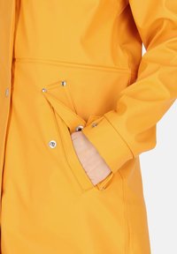 Yellow waterproof jacket with smooth texture, snap closures, and angled side pocket. Features a fitted design and long sleeves.