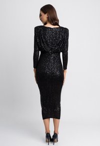Czarna sukienka z cekinami, z długimi rękawami, dopasowaną sylwetką i długością do kolan. Posiada teksturowany materiał oraz marszczenia przy ramionach.
