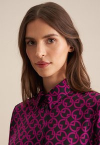 Camicia button-up con un motivo circolare interconnesso che si ripete in rosa acceso su uno sfondo nero, con colletto classico e bottoni neri.