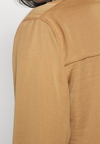 Brown satin blouse with a smooth texture, featuring a classic collar and slightly puffed sleeves. Seam detail along the shoulders.