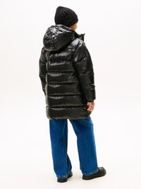 Giacca a vento nera imbottita con cappuccio, realizzata in materiale lucido e con cuciture orizzontali, abbinata a jeans a gamba larga blu e stivali neri.