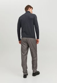 Pull gris foncé avec un col montant, coupe slim, associé à un pantalon rayé gris clair et des chaussures noires, vu de dos.