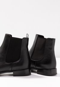 Paire de bottines Chelsea en cuir noir avec panneaux élastiques sur les côtés et languettes de traction, vues de dos sur une surface blanche.