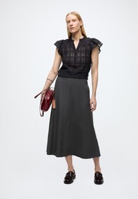 Sort bomullsbluse med volangsleeves, knappestengning; grå, ankel-lang skjørt; burgunderrød skulderveske; mørke fottøy med dekorativ spenne.