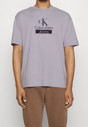 Helles lila Baumwoll-T-Shirt mit dem Calvin Klein Jeans-Logo in dunkelpurpur und grau, mit kurzen Ärmeln und Rundhalsausschnitt.