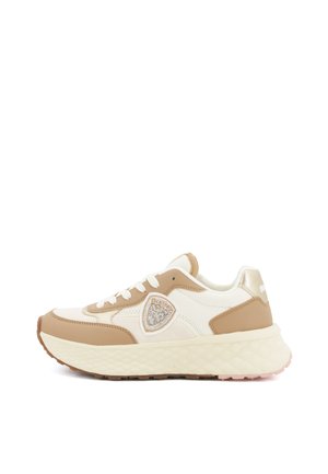 Sneaker beige e crema dal taglio basso con suola spessa e testurizzata, chiusura con lacci frontale e toppa decorativa sul pannello laterale.