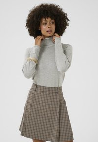 Světle šedý rolák s dlouhými rukávy, kombinovaný s hnědou kostkovanou sukní s záhyby a přiléhavým pasem.