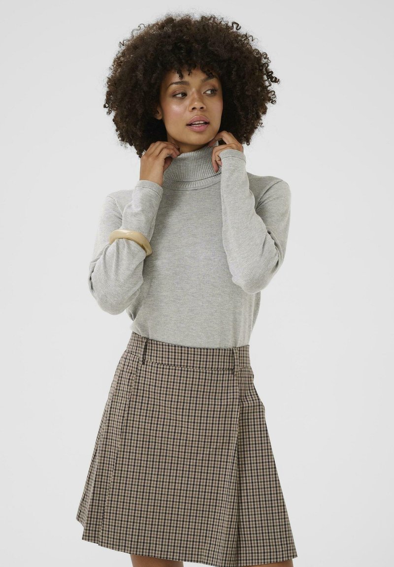 Světle šedý rolák s dlouhými rukávy, kombinovaný s hnědou kostkovanou sukní s záhyby a přiléhavým pasem.