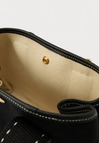 Interno di una borsa di tessuto nero con fodera beige, dotata di una chiusura a scatto dorata e due tasche laterali, bordi cuciti e texture liscia.