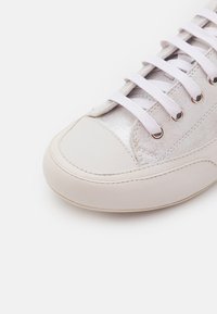 Sneaker bianco con punta in pelle liscia, pannello in tessuto metallico e lacci bianchi piatti infilati attraverso occhielli argentati.