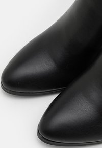 Botas de tobillo de cuero negro con un diseño de punta afilada, textura suave y un tacón bajo y plano. Sin hardware o patrones visibles.
