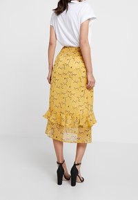 Gonna floreale gialla con orlo arruffato, design a strati e effetto trasparente, abbinata a una semplice maglietta bianca e sandali neri con tacco.
