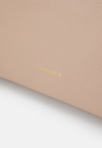 Šviesiai rožinė odinė kuprinė pasižymi subtiliu tekstūru ir aukso "Coccinelle" logotipu. Švarus dizainas be papildomų puošmenų.