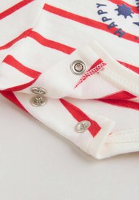 Biało-czerwony pasiasty strój niemowlęcy z otwartym na mankiecie rękawa lub nogawki zapięciem na srebrne zatrzaski, ukazujący teksturę dzianiny i szczegóły szwów.