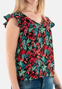 Top à imprimé floral sur fond noir, mettant en avant des fleurs rouges et des feuilles vertes. Tissu doux, design en V et manches volantes.