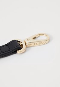 Černý kožený pásek se zlatým kovovým sponou, na které je vygravírované jméno "VALENTINO". Spona má zakřivený design se spouštěcím mechanismem.