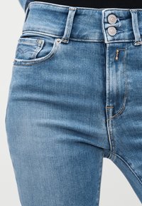 Κοντινό πλάνο ατόμου που φοράει τζιν παντελόνι ανοιχτού μπλε με διπλό κουμπί και λεπτομέρειες ραφής στις μπροστινές τσέπες.