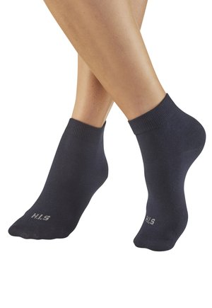 Füße in schlichten dunklen Knöchelsocken mit "H.I.S"-Aufdruck nahe den Zehen, vor weißem Hintergrund gezeigt.