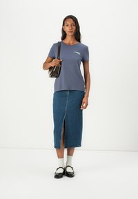 Mørkeblå t-skjorte med korte ermer og logo, kombinert med et mid-length denimskjørt med splitt foran, hvite sokker og kraftige svarte sko.