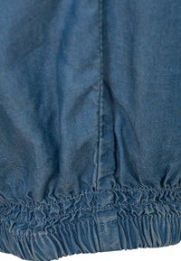 Sininen farkkukangas, jossa on kootut elastiset reunat, esittelee sileän pinnan ja hienovaraiset ompelutiedot sivusaumassa.