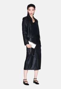 Giacca in pelle nera con motivo trapuntato, top nero aderente, lunga gonna in pelle nera, pochette argento con catena, scarpe nere con cinturino.