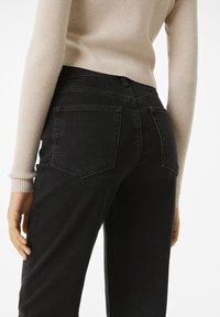 Jeans de mezclilla negra con un corte ajustado, que cuentan con dos bolsillos traseros y una cintura de altura media, combinados con un suéter de punto beis.