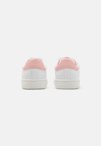 Sneaker bianche con accenti rosa sul tallone, parte superiore in sintetico liscio, suole in gomma testurizzata e fodera verde a contrasto vicino al collo.