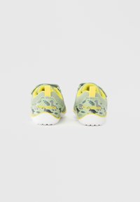 Παιδικά αθλητικά παπούτσια με άνω μέρος από διαπνέον πλέγμα σε πράσινο χρώμα, με κίτρινες λεπτομέρειες και παιχνιδιάρικα μοτίβα δεινοσαύρων στα πλαϊνά και την πίσω πλευρά.