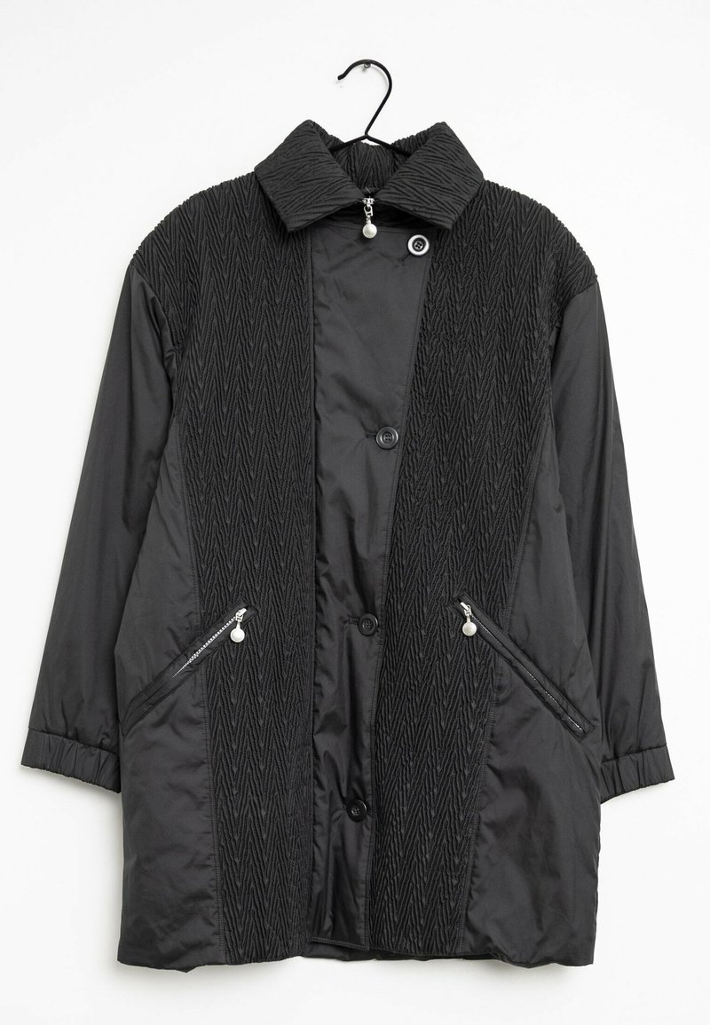 Svart jacka med en strukturerad framsida med zickzackmönster, två fickor med dragkedja och en nedfällbar krage. Framdela med knappar och en mjuk yta.