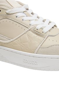 Baskets beige et blanches avec des lacets blancs, des panneaux en suède et en cuir, un logo embossé, et la marque "COLUCCI" sur la semelle.