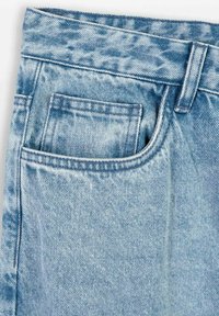 Wybledziałe niebieskie dżinsy z pętlą na pasek i widocznymi szwami kieszeni z przodu w górnej części bioder.