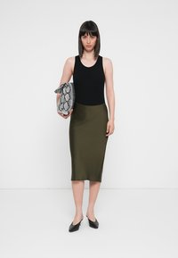 Black sleeveless top paired with a fitted olive green midi skirt. Holding a black and white snake print clutch. Black flats worn.