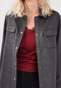 Ciemnoszary, zapinany na guziki żakiet z dwoma kieszeniami na piersiach, wykonany z teksturowanej tkaniny. Nosi się go na głęboką czerwoną koszulę na ramiączkach z koronkowym wykończeniem.