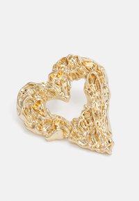 Guld hjärtformat brosch med en texturerad, organisk design; polerad yta reflekterar ljus; öppen mittdel framhäver formens detaljer.