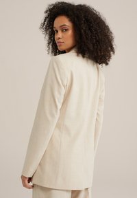Beige skræddersyet blazer med en struktureret silhuet, subtil tekstur og klippede revers. Har en ventilation bagpå og lange ærmer.