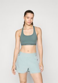 Sujeción deportiva en un verde apagado con una banda ancha etiquetada como "BORG". Combinada con pantalones cortos de un verde claro que cuentan con una cinturilla elástica y una textura suave.