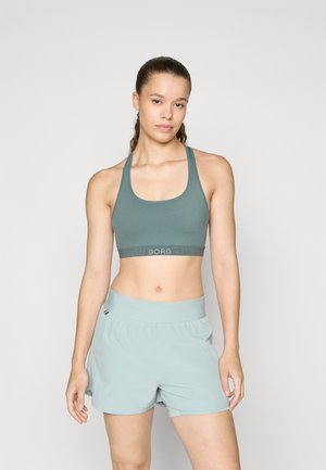 Sports bra in muted green with a wide band labeled "BORG." Paired with light green shorts featuring an elastic waistband and smooth texture.