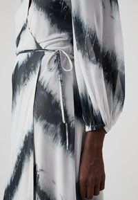 Maxi šaty z lehkého materiálu, s tie-dye vzorem v odstínech černé a bílé, s nařaseným pasem a dlouhými volnými rukávy.