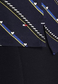 Tessuto a motivi navy con strisce diagonali gialle e blu, piccoli cuori bianchi e un accento rosso. Texture liscia con bordi puliti.