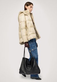 Beige puffjacka med huva, ribbad textur. Mörkbruna läderhandskar. Blå denim cargobyxor. Stor svart läderväska med gulddetalj.