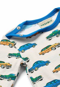 Bílý overal z látky s barevnými vzory vintage aut v modré, zelené, oranžové a žluté. Rámovaný modrou barvou u krku a s patentkami.
