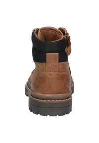 Bruine leren enkelboot met een zwart gewatteerd kraagje, dikke zwarte rubberen zool en een rits aan de zijkant, gezien vanaf de achterkant.