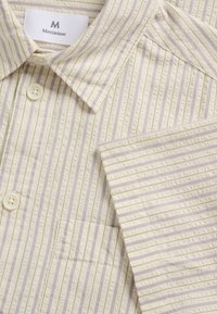 Chemise crème claire avec rayures verticales lavande, tissu texturé, boutons blancs, col pointu et poche poitrine, étiquette de marque "Matinique".