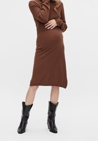 Brun stickad klänning med krage och långa ärmar, med en figurnära silhuett som går nedanför knäna, i kombination med svarta cowboystövlar.