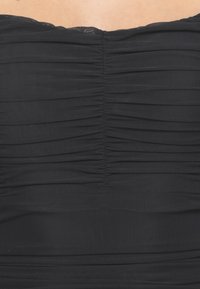 Haut noir sans bretelles avec un design plissé. Texture lisse, détails froncés au centre et finition sans couture. Légère brillance sous la lumière.