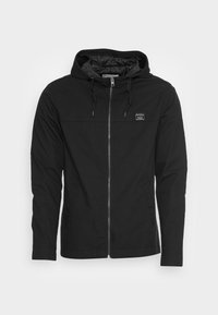 Giacca nera con cappuccio e zip frontale, realizzata in tessuto leggero. Caratterizzata da una tasca sul petto con zip e cappuccio con coulisse, ha una texture liscia.