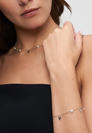 Silbernes Gliederarmband mit zwei Perlakzenten und kleinen dreieckigen Anhängern; glatte Metallstruktur mit polierter Oberfläche; elegantes Design.